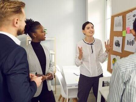 Twee vrouwen en twee mannen staan voor een prikbord en overleggen met elkaar